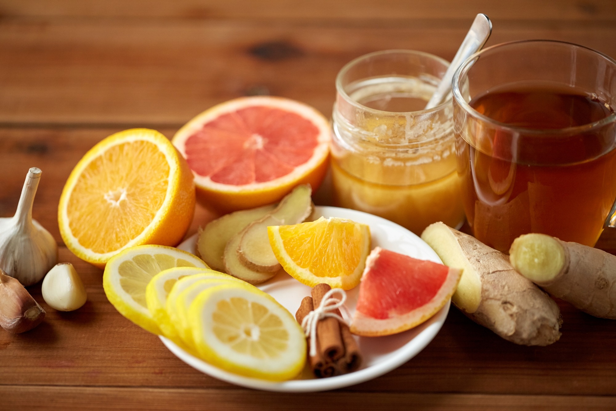 Health, traditional medicine, folk remedy and ethnoscience concept - cup of ginger tea with honey, citrus and garlic on wooden background