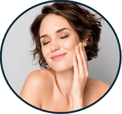 A woman with short, curly hair smiles gently while touching her face, conveying a sense of beauty and self-care. This image highlights skincare and wellness themes.