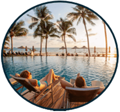 Couple relaxing by a serene pool at sunset, surrounded by palm trees and ocean, highlighting a tranquil vacation atmosphere.